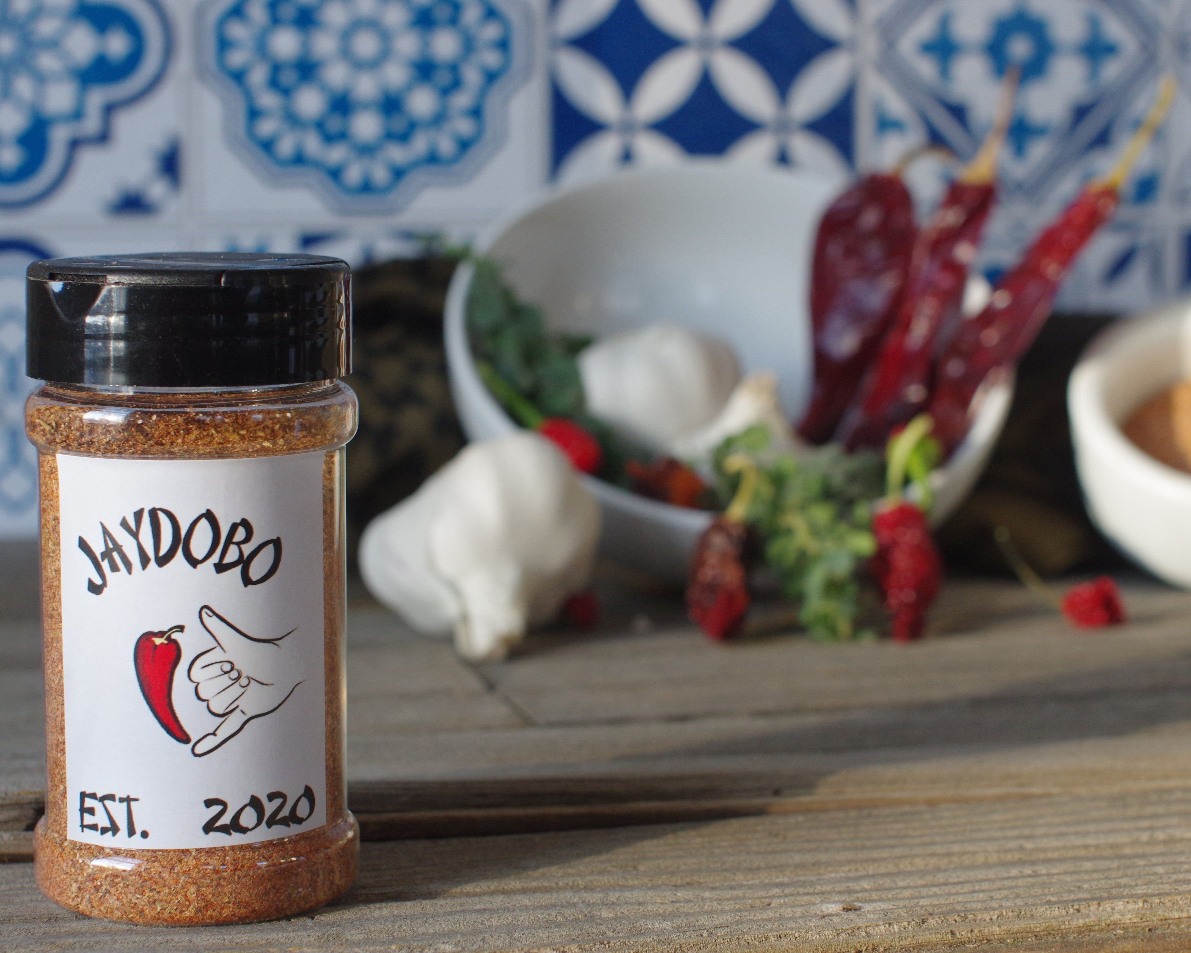 Jaydobo's classic spice blend positioned in front of ingredients. Featured ingredients are dried Carolina Reaper peppers and garlic bulbs.